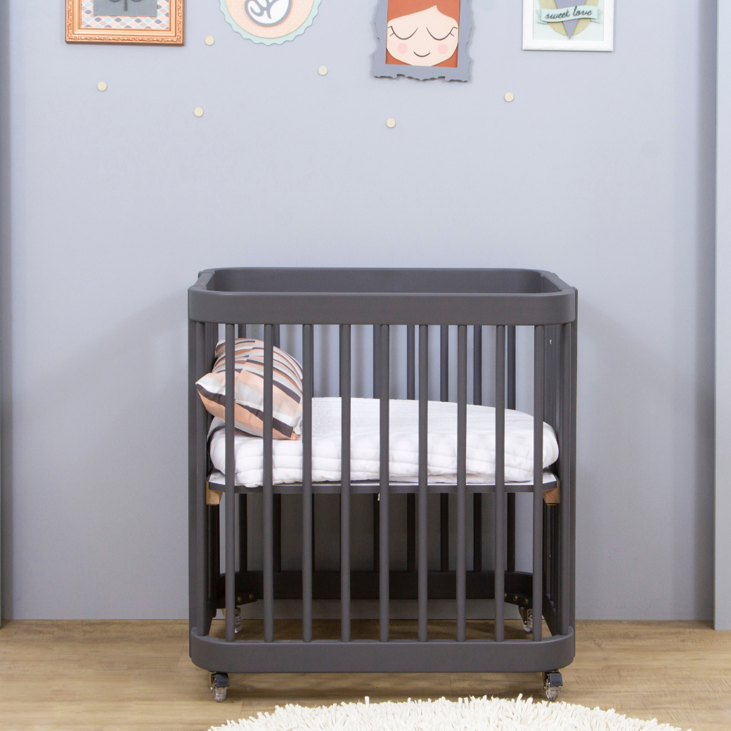 Mini berço em um quarto de menina. Parede em tons lilás com quadros, chão em madeira