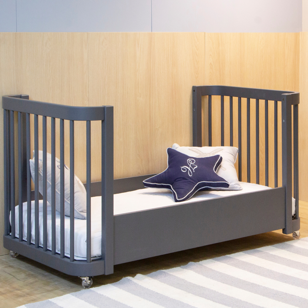 Mini cama em um ambiente neutro. Almofadas em tom branco e azul em cima do móvel, com um tapete listrado branco com azul