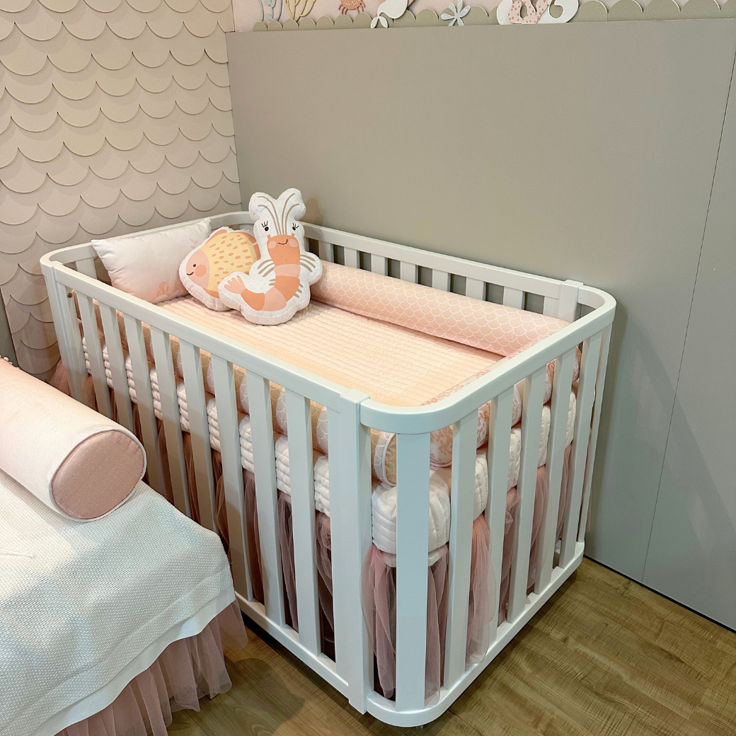 Berço Loop Branco em um quarto de menina tema mar. Dentro do berço há uma almofada de peixe e uma de caranguejo